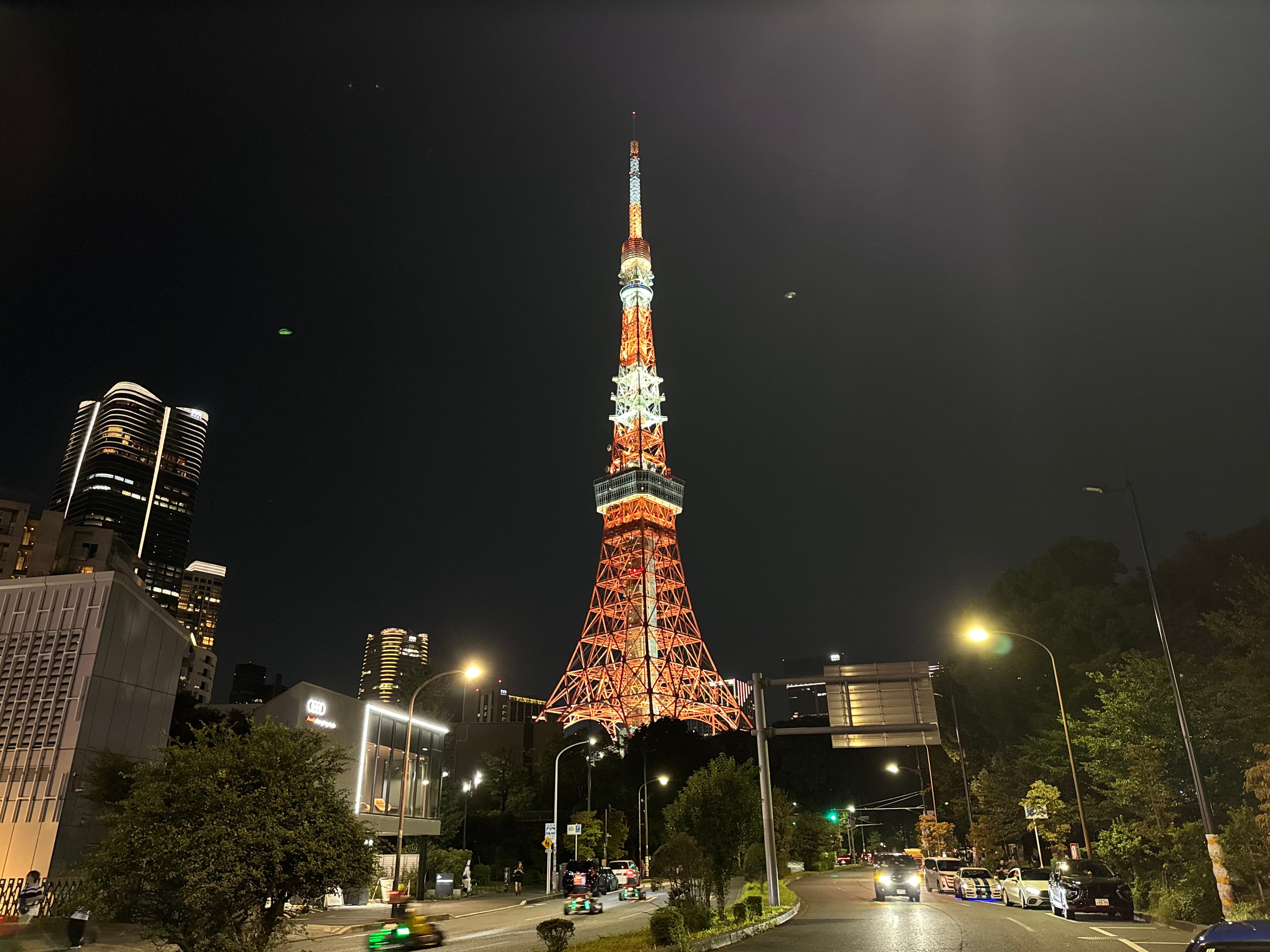 Tokyo Tower illuminated in orange and white above a street in central Tokyo at night